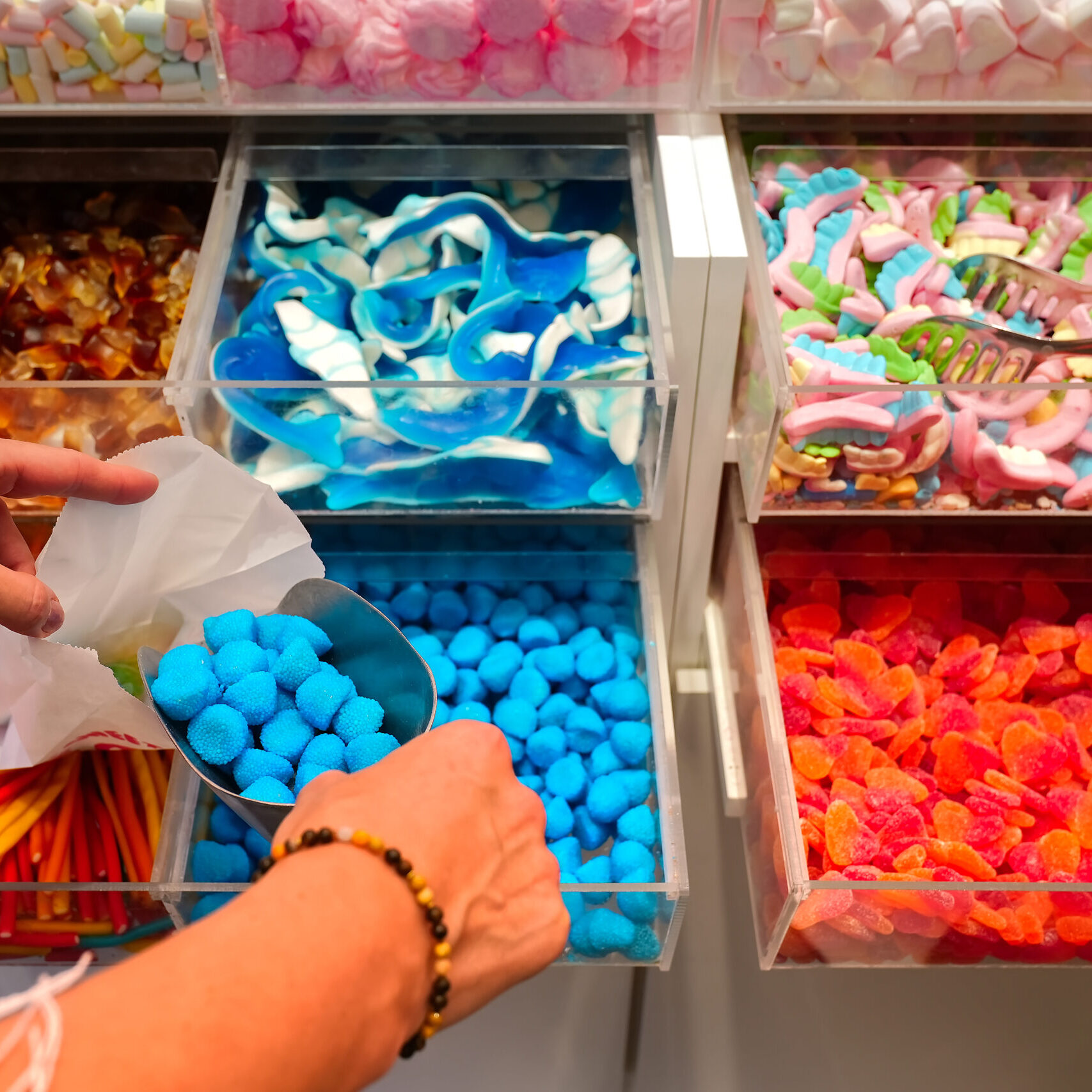 candy store. Woman hand with scoop taking colorful delicious candies on counter of shop, grocery, market, cafe. Many colorful candies on grocery stand Dessert, sale, sweet food and confectionery concept.